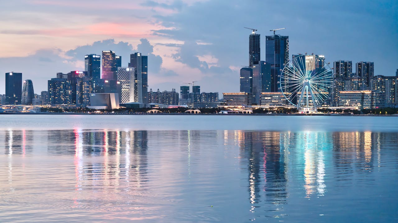 About Beautiful city skyline at sunset reflecting on the calm water, featuring a prominent Ferris wheel.